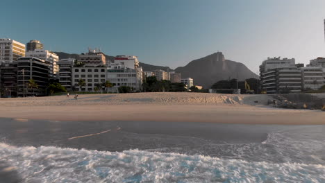 Luftanflug-Auf-Den-Strand-Von-Leblon-In-Rio-De-Janeiro-Bei-Sonnenaufgang,-Gesehen-Von-Den-Wellen,-Die-Das-Ufer-Erreichen