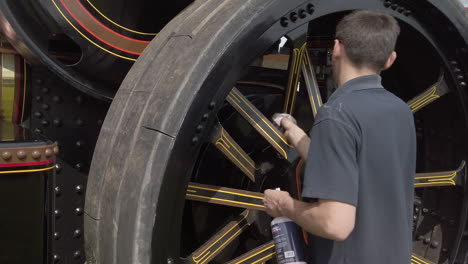 A-man-cleaning-the-rear-wheel-of-a-black-vintage-traction-engine-with-a-cloth