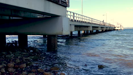 Toma-En-ángulo-Bajo-Del-Embarcadero-De-Woody-Point-Con-Olas-Rompiendo-En-Una-Mañana-Fría-Y-Soleada