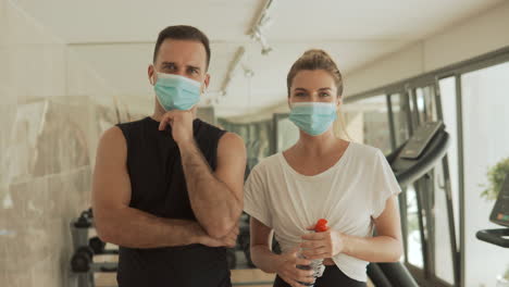 Young-athlete-female-and-male-with-face-mask-looking-to-camera-in-the-gym.-Sport-during-the-COVID-19-pandemic.