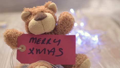 Süßer-Teddybär-Mit-Frohen-Weihnachtsgrüßen-Und-Blinkenden-Lichtern-Im-Hintergrund
