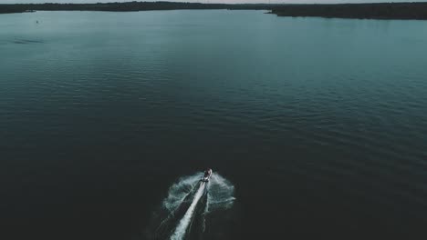Aerial-drone-shot-of-a-jetski-riding-in-the-middle-of-a-lake,-slow-pan-up-to-reveal-sunset-skies