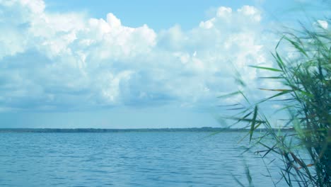 Time-lapse-of-beautiful-white-fast-moving-puffy-cumulus-clouds-over-the-lake-Liepaja-in-sunny-summer-day,-wide-low-angle-shot