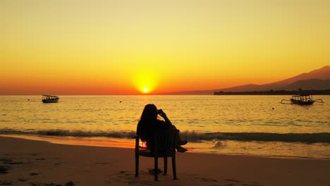 Silhouette-Eines-Mädchens,-Das-Bei-Sonnenuntergang-Am-Strand-Sitzt-Und-Sein-Smartphone-Nutzt