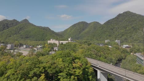 Short-aerial-pan-shot-revealing-beautiful-mountainous-scenery-in-Jozankei-famous-hot-spring-onsen-town-Hokkaido,-Japan