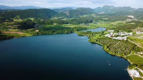 Aerial-ascending-landscape-shot-of-coast-of-lake-velenjsko-with-hills-in-the-background-slovenia-europe