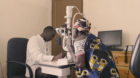 Médico-Africano-Revisando-La-Vista-Del-Paciente-En-El-Hospital-Oftalmológico-Y-El-Médico-Moviendo-El-Equipo-Y-Colocando-La-Cabeza-Del-Paciente-En-El-Lugar-Correcto-Para-Los-Ajustes