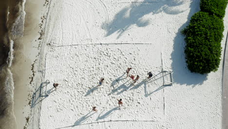 People-playing-soccer-at-Cancun-beach-with-white-sand,-sea-wrack,-algae-and-the-resort-next-to-them,-from-a-drone-perspective