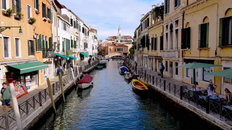 Sight-of-the-market-showing-people-walking-on-the-paths-beside-the-canal-of-Venice,-Italy