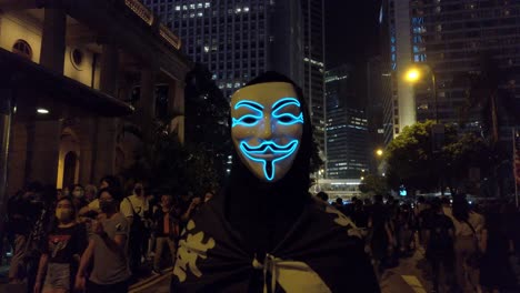 Langsamer-Vorstoß-Eines-Demonstranten-Mit-Guy-Fawkes-Maske,-Während-Eine-Menschenmenge-In-Hongkong-Vorbeiläuft