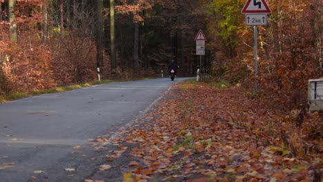 Biker-with-black-helmet-drives-on-a-street-through-a-autumnally-forest