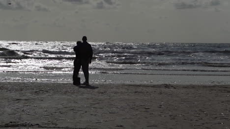 Romantische-Silhouette-Eines-Paares-Am-Strand-Und-Wellen,-Die-Vom-Meer-Kommen