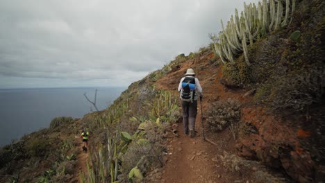 A-female-hiker-walks-on-a-small-rocky-path-with-view-over-the-ocean-in-Anaga-mountains-on-Tenerife