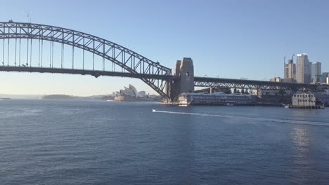 Sydney-Harbour-Bridge,-Australia-|-4K-UHD-Stunning-drone-shot-of-a-boat-travelling-under-the-Harbour-Bridge-at-Sunrise