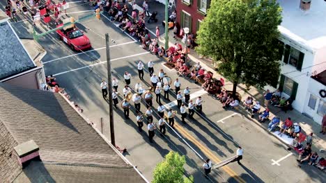 Primer-Plano-Aéreo-De-La-Banda-De-Música-Durante-El-Desfile-En-Un-Pequeño-Pueblo-De-América,-La-Gente-Se-Alinea-En-Las-Aceras