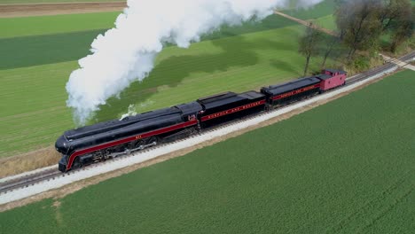 Aerial-view-of-an-antique-restored-steam-locomotive-traveling-thru-countryside-as-it-is-blowing-white-smoke-and-steam