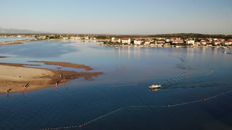 Aerial-panorama-of-a-Nin-town-with-lagoon-and-boat-approaching-in-sunset
