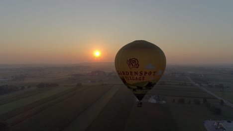 Sunrise-of-a-Hot-Air-Balloon-on-a-Misty-Morning-Over-Amish-Farmlands-as-Seen-by-a-Drone