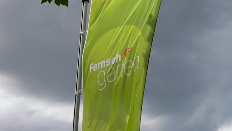 Zdf-Fernsehgarten-Green-Flag-On-A-Windy-Cloudy-Day,-Wiesbaden,-Germany