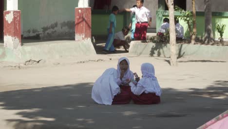 Eine-Gruppe-Muslimischer-Schulmädchen-Sitzt-Auf-Dem-Schulhof-Und-Unterhält-Sich-In-Einem-Ländlichen-Dorf-In-Indonesien