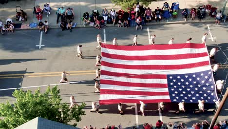 Eine-Luftaufnahme-Von-Amerikanischen-Pfadfindern-Mit-Flagge-Bei-Der-Parade,-Pfadfinder-Folgen,-Jubelnde-Menschenmengen-Entlang-Der-Straße-Auf-Dem-Bürgersteig