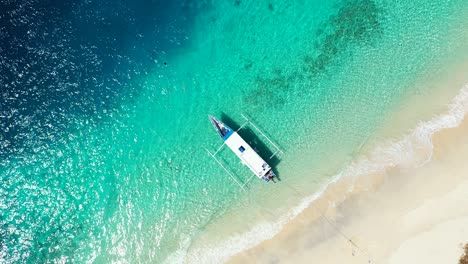 Boat-anchored-on-shore-of-tropical-island-with-pristine-sandy-beach-washed-by-clear-emerald-water-of-blue-turquoise-sea,-Caribbean
