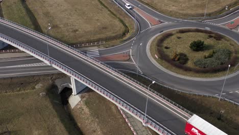 Aerial-wide-angle-fly-by-shot-of-the-traffic-on-a-highway-ring-road-roundabout-on-a-bright-sunny-afternoon