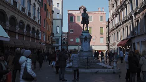People-commuting-around-Carlo-Goldoni-statue,-a-monument-to-the-finest-comedy-playwright-from-Italy