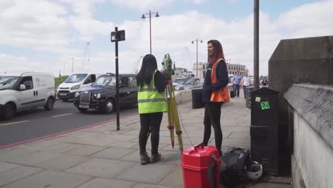 Two-surveyors-girls-talking-during-work,-traffic-jam-in-background,-London-city