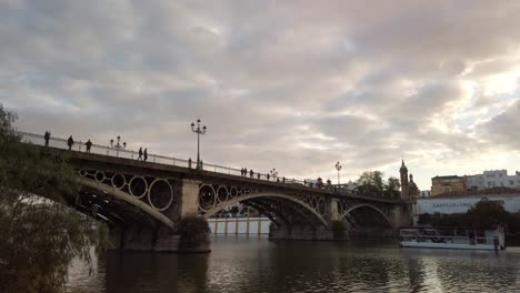 Silhouette-People-on-Triana-Bridge-and-Tour-Boat-on-Guadalquivir-River,-Seville