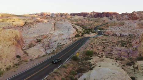Black-Ferrari-sports-car-driving-through-the-Valley-of-Fire,-Nevada,-USA,-at-sunset