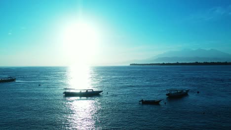 Romantic-sunset-with-glowing-sun-in-clear-sky-reflecting-sunlight-on-calm-bay-with-boats-floating-near-shore-of-tropical-island,-Bali