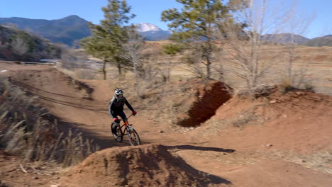 Man-jumping-dirt-ramps-on-an-obstacle-course-trail-in-Colorado-Springs,-Colorado