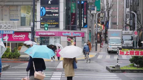 Peatones-Con-Paraguas-Cruzando-Un-Paso-De-Peatones-Bajo-La-Lluvia-En-El-Centro-De-Tokio,-Japón