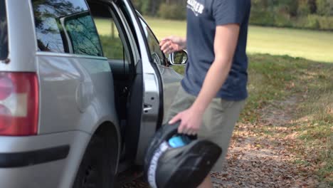 Young-man-is-walking-to-his-car-and-taking-out-is-helmet-from-the-backseat