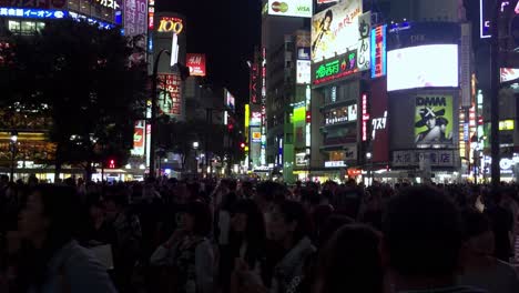 Shibuya-crossing-with-thousands-of-people-crossing-at-night-with-illuminated-billboards,-handheld-shot