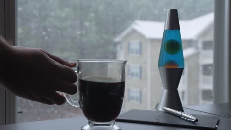 La-Mano-Coloca-Una-Taza-De-Café-De-Cristal-Nevando-Fuera-Del-Apartamento-De-La-Oficina-En-Casa-A-Cámara-Lenta