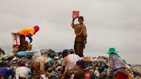 A-young-boy-stands-on-a-pile-of-garbage-in-a-dump-while-others-scavenge-around-him