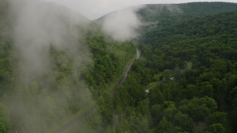 Aerial-drone-flying-through-white-rainy-fog-to-show-curvy-mountain-road-in-dense,-green-forest-in-central-Pennsylvania