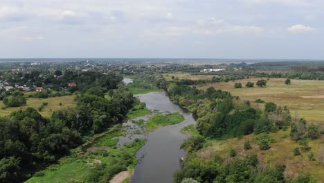 Vista-Aérea-De-Un-Río-Bordeado-Por-Campos-Fuera-De-Un-Pequeño-Pueblo-En-Ucrania