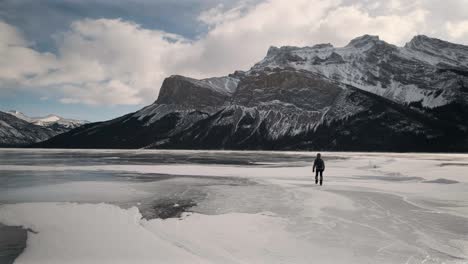Person-is-Epic-Hiking-on-a-Frozen-Alpine-Lake,-Handheld-Wide-Angle-Sun