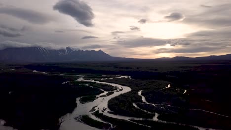 Sunset-picturesque-landscape-scene-above-Dezeadeash-River-meandering-in-forest-with-rough-rugged-rocky-Saint-Elias-mountain-range-in-background-on-cloudy-sky-day,-Yukon,-Canada,-overhead-aerial