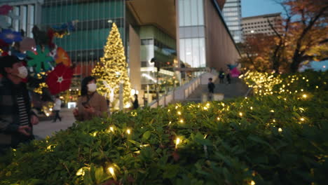 Japanese-Couple-In-Masks-With-Glowing-Christmas-Lights-Around---Christmas-2020-In-Tokyo---medium-shot,-slow-motion