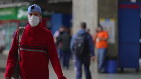 Young-Brazilian-guy-walking-out-in-public-wearing-medical-face-mask,-Covid-19-pandemic