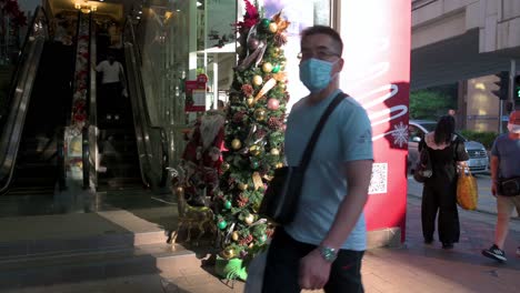 Peatones-Con-Máscaras-Faciales-Pasan-Frente-A-Una-Tienda-De-Flores-Y-Productos-De-Decoración-Para-El-Hogar-Con-Un-árbol-De-Navidad-Y-Adornos-Expuestos-En-Su-Entrada-En-Hong-Kong