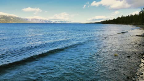 Waves-washing-on-shore-of-Atlin-lake-with-white-peak-mountain-in-background,-British-Columbia,-Canada