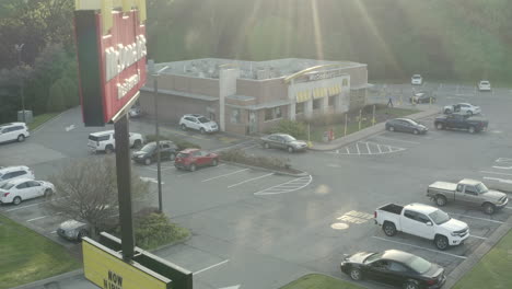 Drohnen-Luftrückzug-Vom-Parkplatz-Des-McDonald&#39;s-Restaurantgebäudes-Mit-Schild-Bei-Sonnenaufgang,-Das-Rückwärts-Fliegt