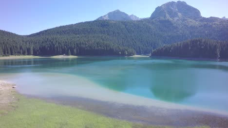 Clean,-green,-lake-water-with-mountain-tops-and-forest-all-around