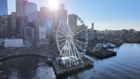 Sun-shining-through-the-city-skyline-of-Seattle-and-Illuminating-the-Great-Wheel,-aerial-orbit