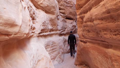 Young-man-walking-in-orange-rock-passage-in-Valley-of-Fire-State-Park,-Nevada,-USA